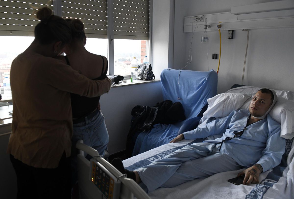 Juan Diego se recupera en la cama de su habitación del Virgen de la Arrixaca mientras dos de sus familiares se abrazan frente a él.