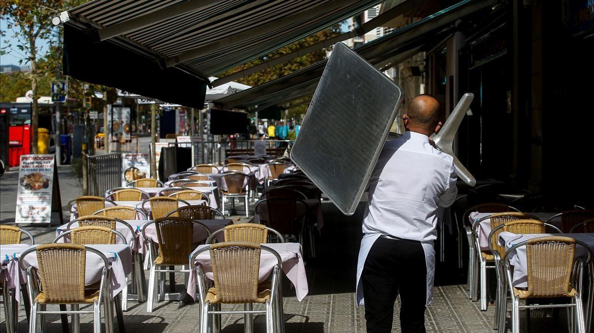 GRAFCAT3088  BARCELONA  15 10 2020 - Un camarero recoge una mesa de una terraza de un restaurante del barrio de la Barceloneta de Barcelona  este jueves  a la espera de que manana entre en vigor el cierre de bares y restaurantes durante 15 dias y las nuevas restricciones de aforo en centros comerciales  comercios  gimnasios  teatros y cines que ha aprobado el gobierno catalan para intentar contener los contagios de coronavirus  EFE Quique Garcia