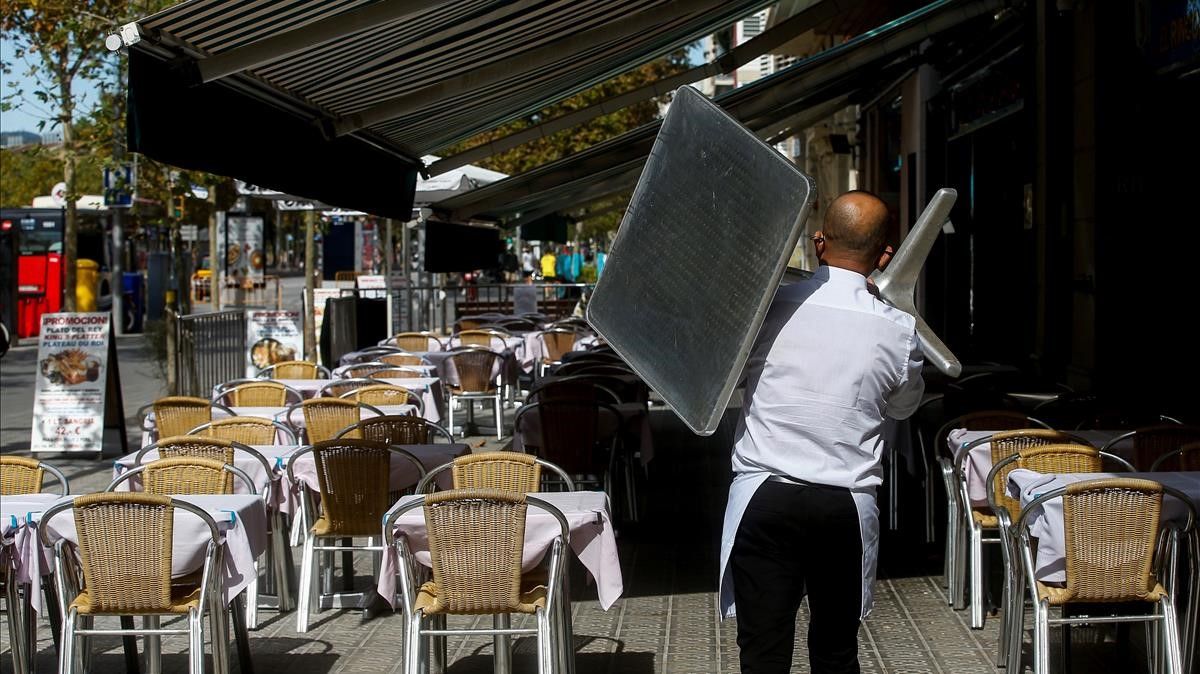 Un camarero recoge una mesa de una terraza de un restaurante del barrio de la Barceloneta.