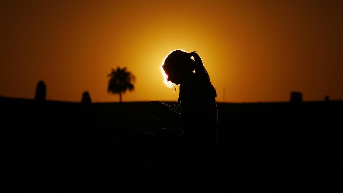 Una mujer observa el atardecer sentada en la ribera del río Guadalquivir, en Córdoba