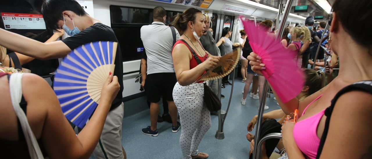 Usuarios de la L1 del metro de Barcelona se abanican para paliar los efectos del calor.