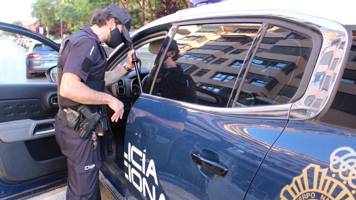 Archivo - Un agente de la Policía Nacional junto a un coche patrulla