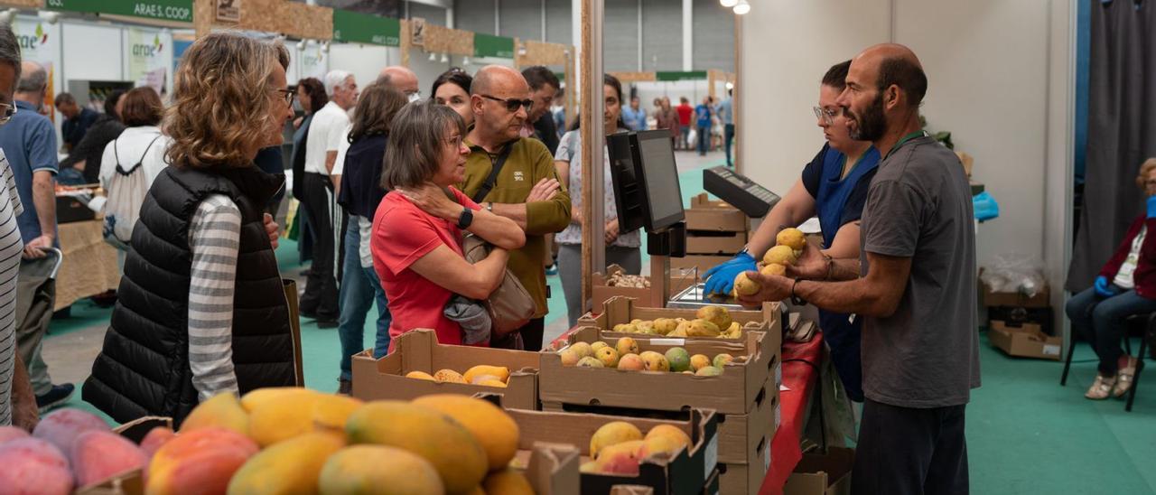 Varios asistentes a la feria se interesan por los productos de una frutería. |