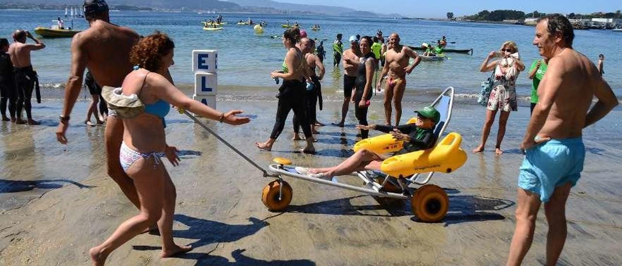 Varios bañistas ayudan a una persona afectada de ELA a desplazarse en la silla anfibia en Rodeira. // G.N.