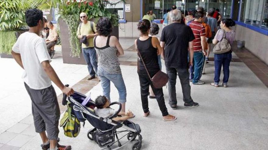 Una hilera de personas hace cola a la espera de ser atendidos en la oficina del cheque social .  // M. G. Brea