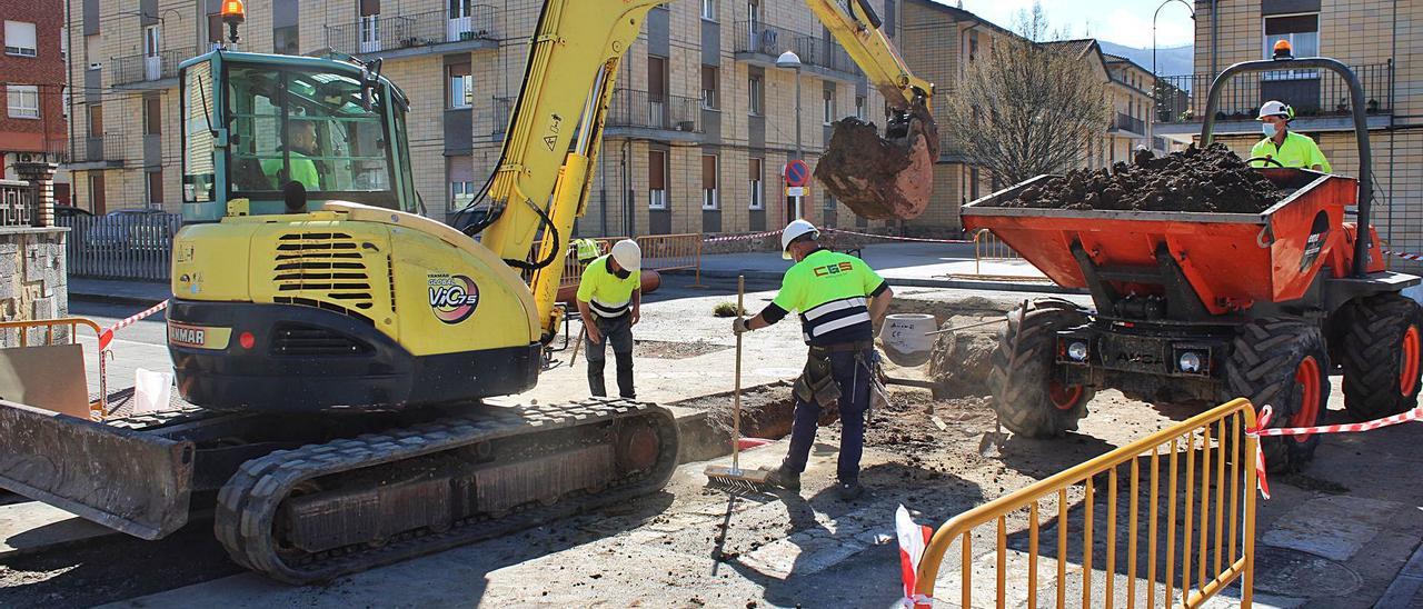 Las obras del saneamiento que se están llevando en cruce entre las calles Juan XXII y Luis Alonso. Arriba a la derecha, material para los trabajos acumulado en la primera de estas dos calles, junto a la iglesia de Pola de Laviana. | L. M. D.