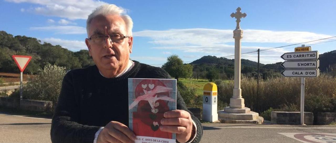 Josep Grimalt Vidal muestra el libro ante la recientemente limpiada cruz de término.