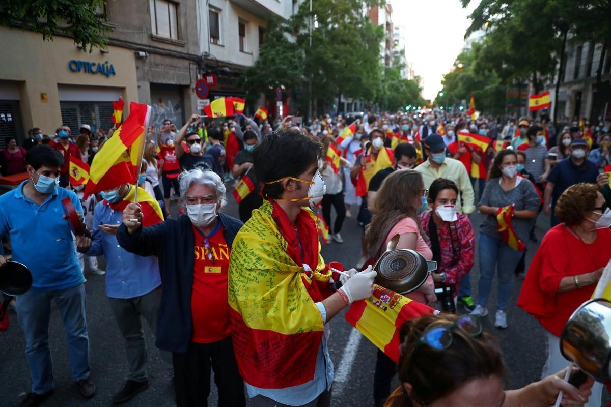 People wearing protective face masks bang saucepans and carry Spanish flags as they attend a protest against the Spanish government’s handling of the coronavirus disease (COVID-19) crisis, outside the headquarters of the ruling Spanish Socialist Workers Party (PSOE) party, in Madrid, Spain, May 18, 2020. REUTERS/Sergio Perez