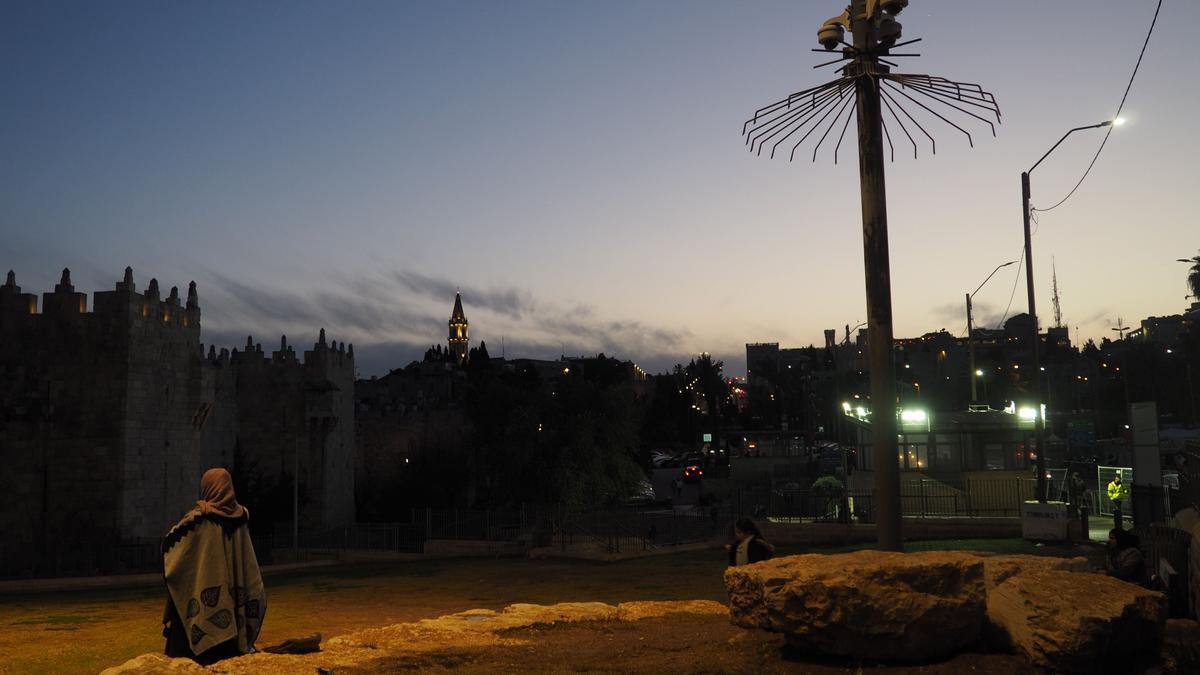 Una mujer palestina reza al atardecer frente a multitud de cámaras en la Ciudad Vieja de Jerusalén.