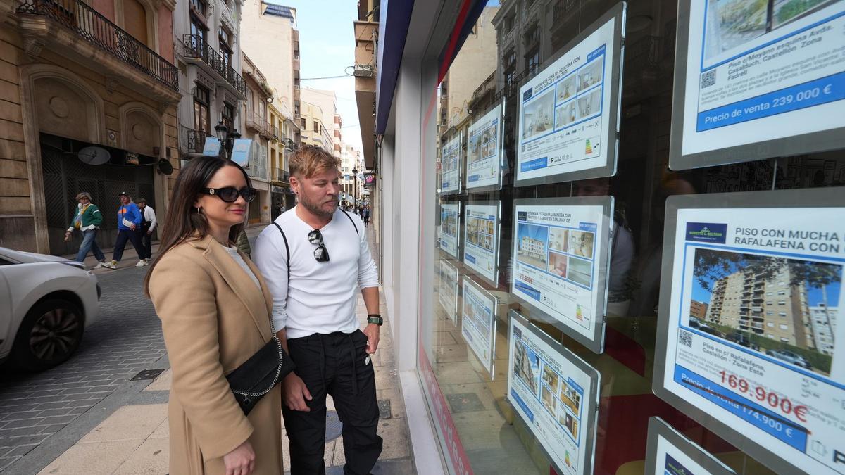 Dos jóvenes miran los carteles de una inmobiliaria en Castelló.