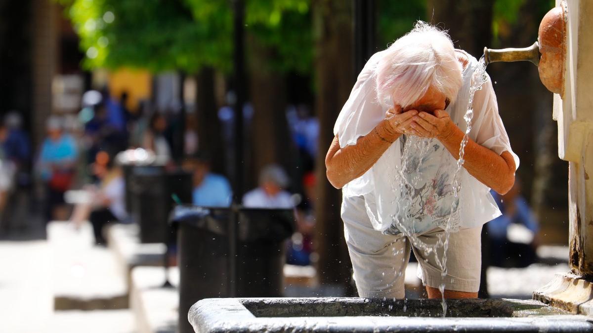 Una dona refrescant-se la cara en una font pública.