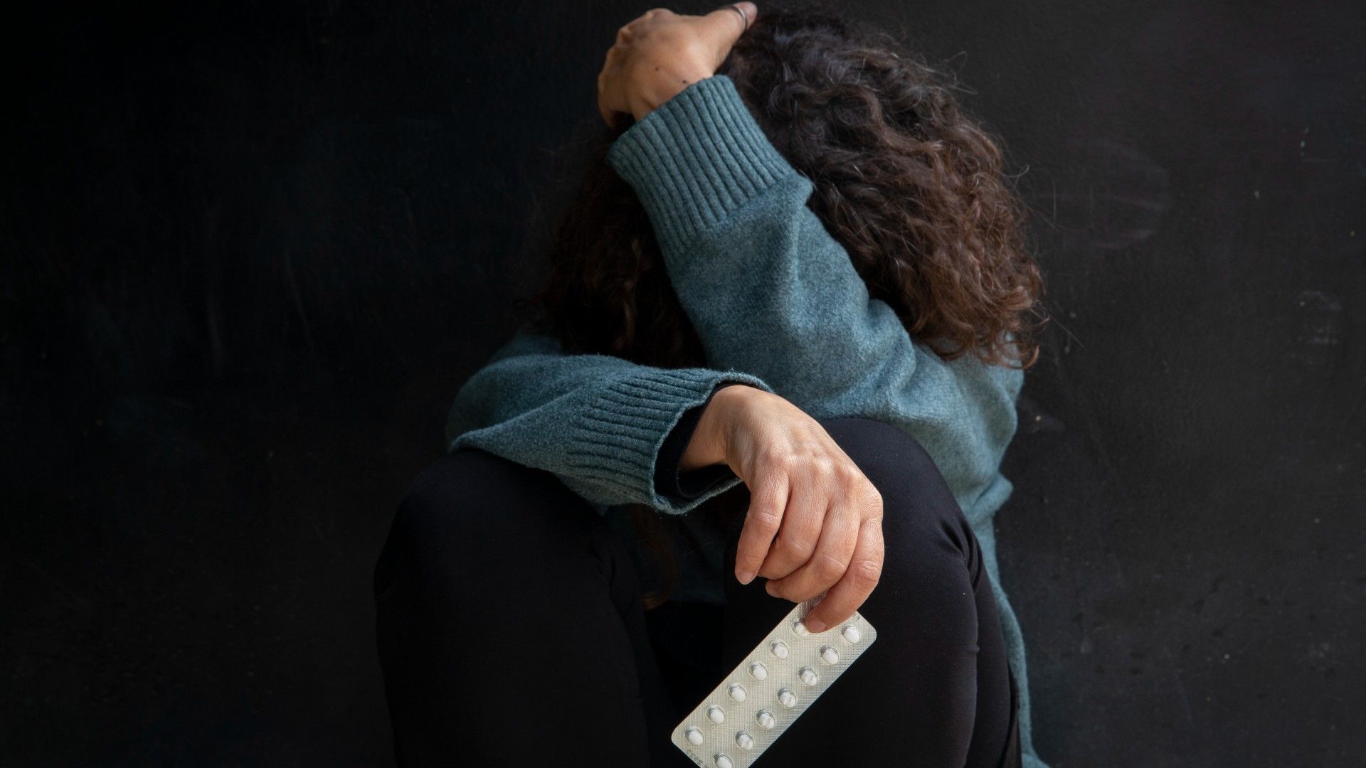 Una mujer se tapa mientras sostiene un blíster de pastillas en la mano