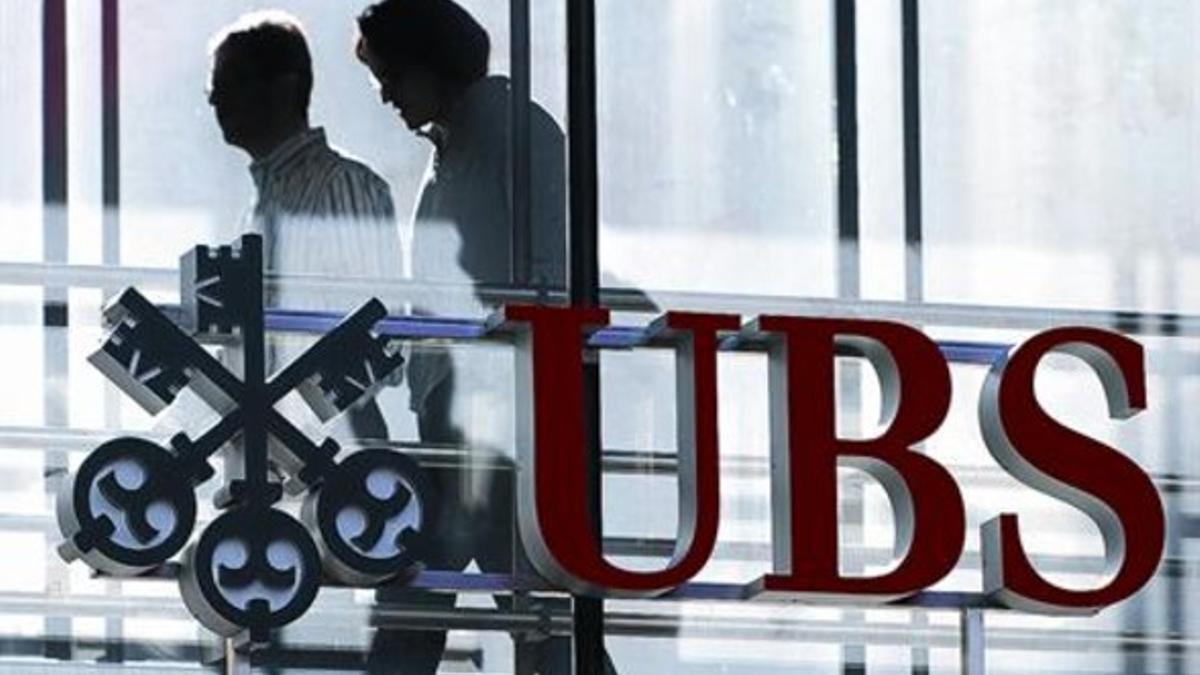 Unos trabajadores pasean tras el logotipo del banco UBS, en su sede suiza.