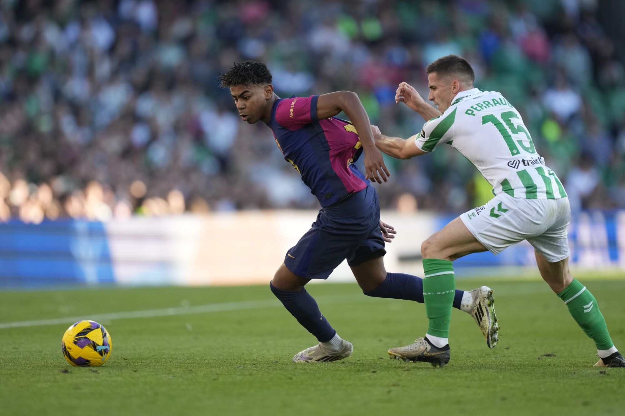Barcelona's Lamine Yamal, left, challenges for the ball with Betis' Romain Perraud during a Spanish La Liga soccer match between Betis and Barcelona at the Benito Villamarin stadium in Seville, Spain, Saturday, Dec. 7, 2024. (AP Photo/Jose Breton)