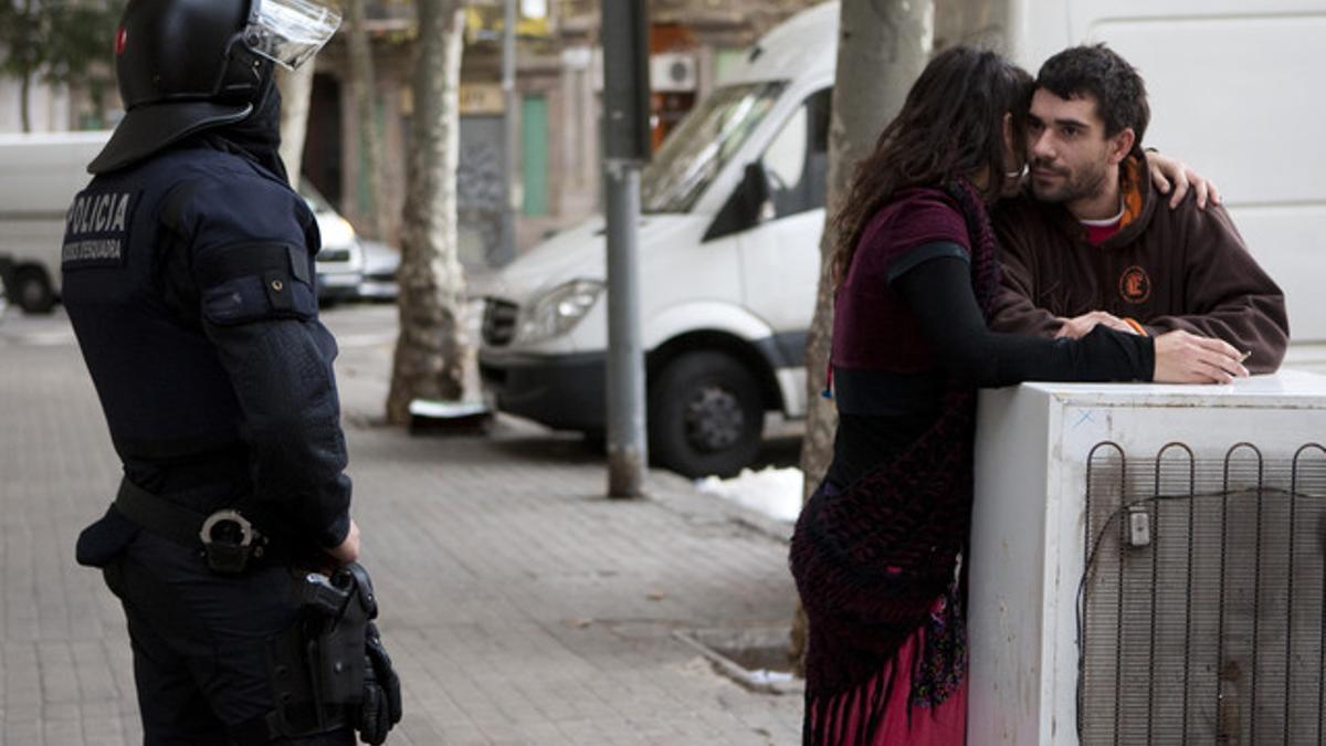 Dos okupas conversan ante la mirada de un agente, hoy, en Barcelona.