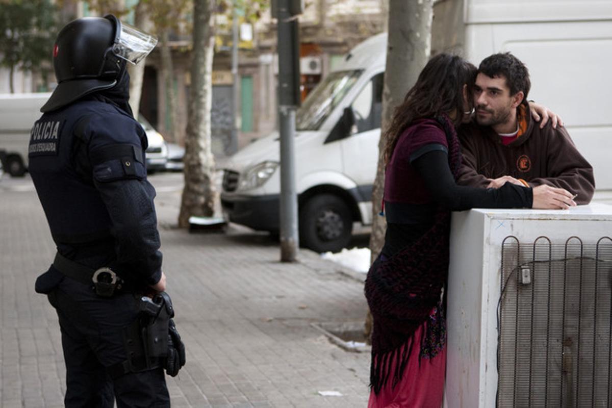 Dos okupes conversen davant la mirada d’un agent, avui, a Barcelona.