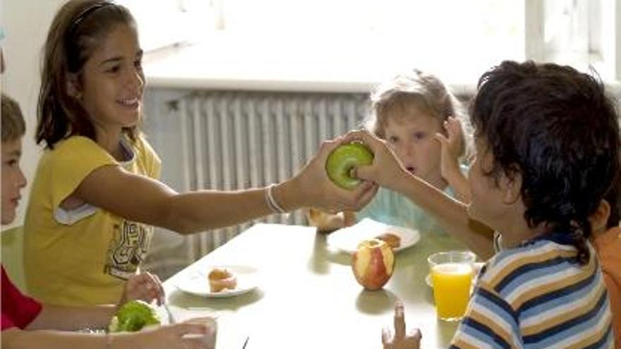 Niños en el comedor se pasan una manzana mientras otros beben zumo.