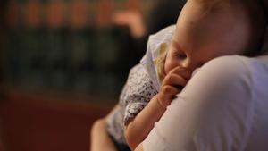 Un bebé dormido en brazos de una mujer.