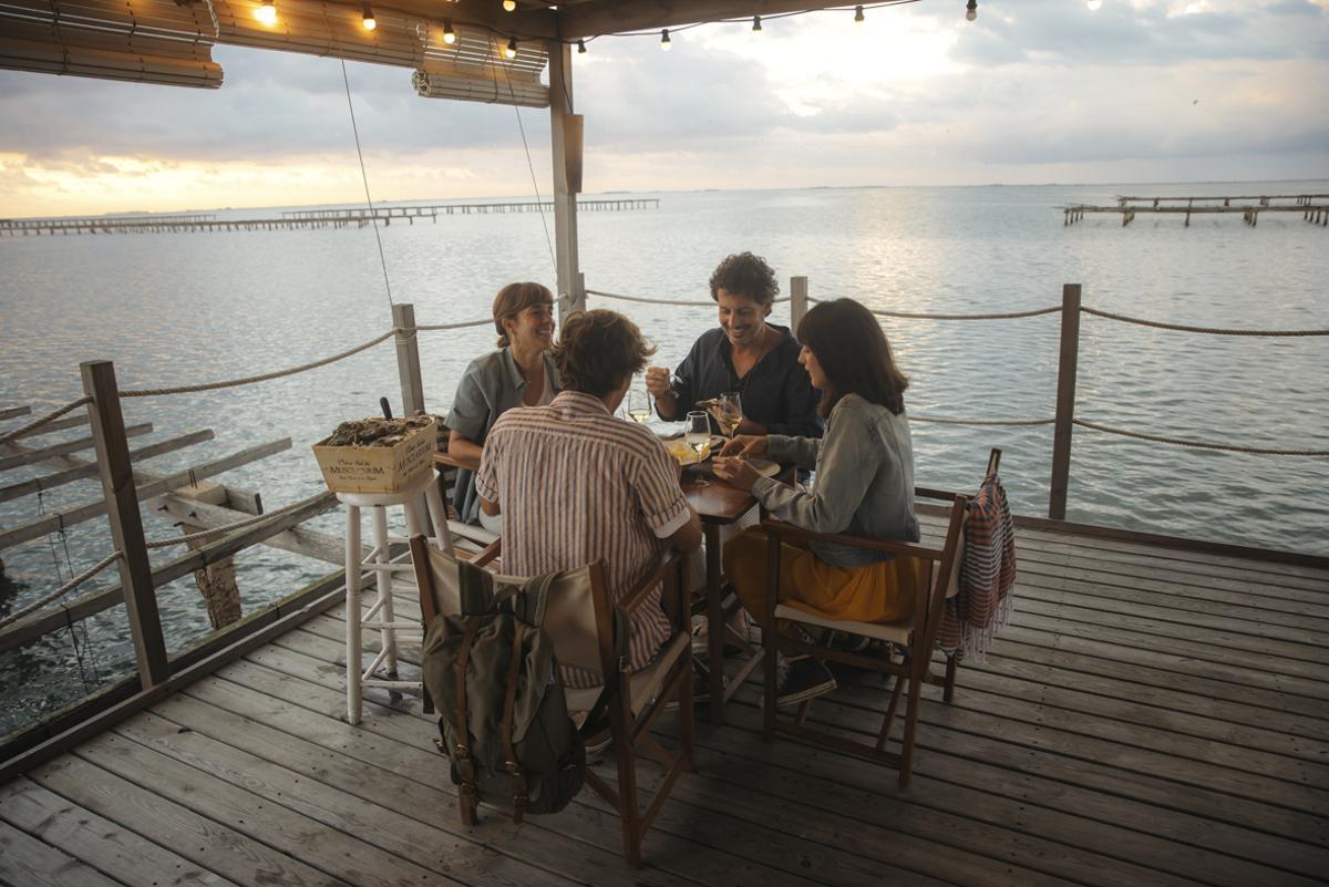 Un grupo de amigos disfrutando del vino durante una comida junto al mar. 