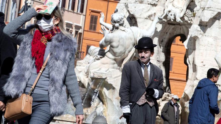 Un hombre disfrazado de Charles Chaplin observa a los transeúntes con máscaras sanitarias en Roma.