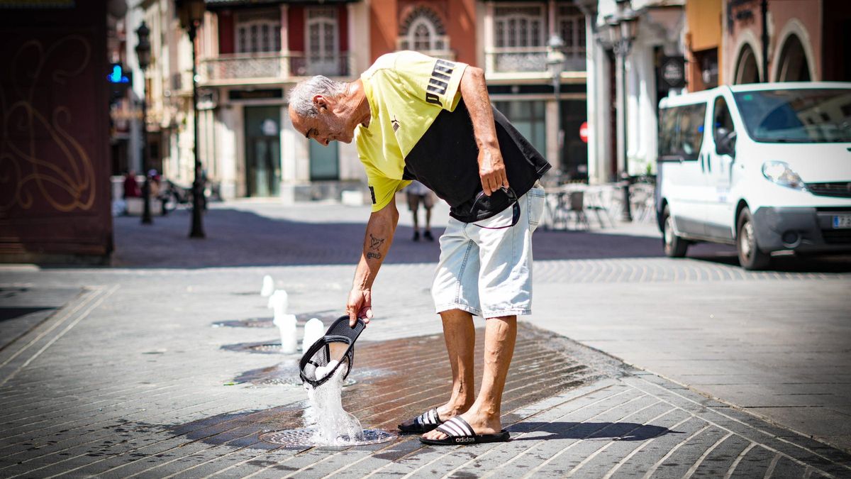 Una persona sin hogar moja su gorra en una fuente de la plaza de la Soledad de Badajoz para refrescarse.