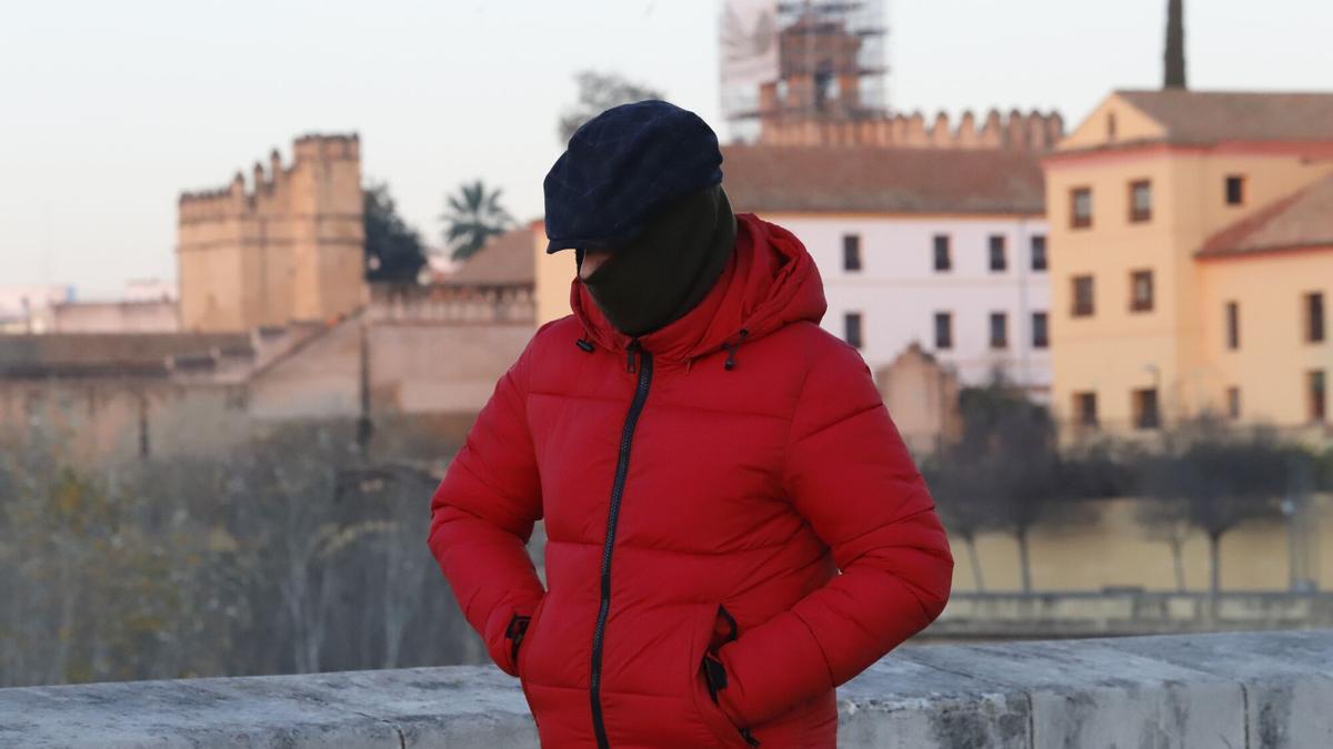 Un hombre camina por el Puente Romano de Córdoba con abrigo, gorro y bufanda.