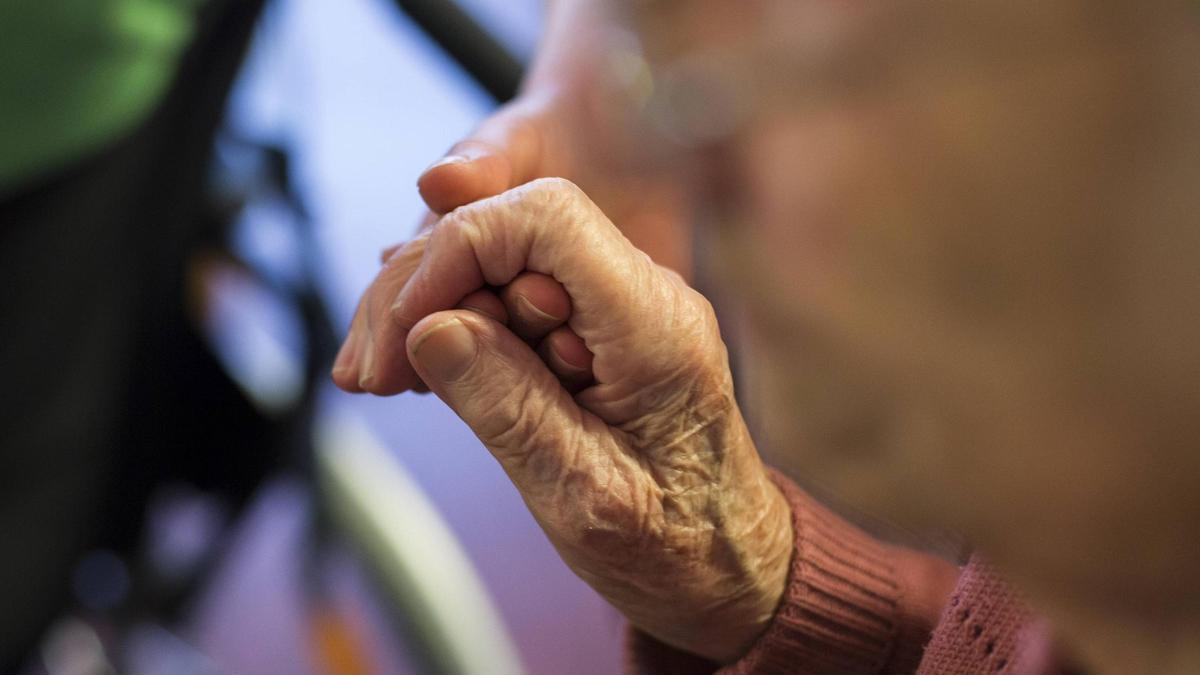 Una sanitaria sujeta las manos de una mujer anciana.