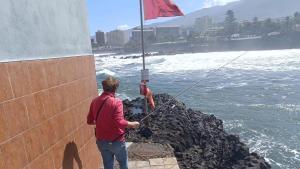 Una persona se acerca a la costa de Puerto de la Cruz, en Tenerife, para pescar en plena alerta y sin respetar una bandera roja.