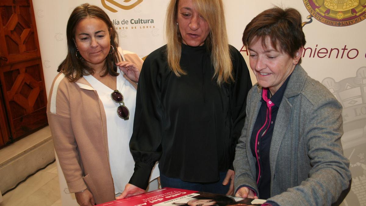 Eva Terrer, María Ángeles Mazuecos y María Dolores Chumilla, contemplan el cartel del concierto.