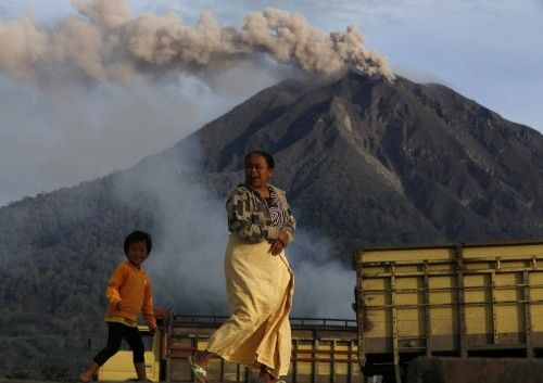 A mother with her son walk as Mount Sinabung spews ash as seen from Tiga Pancur village in Karo