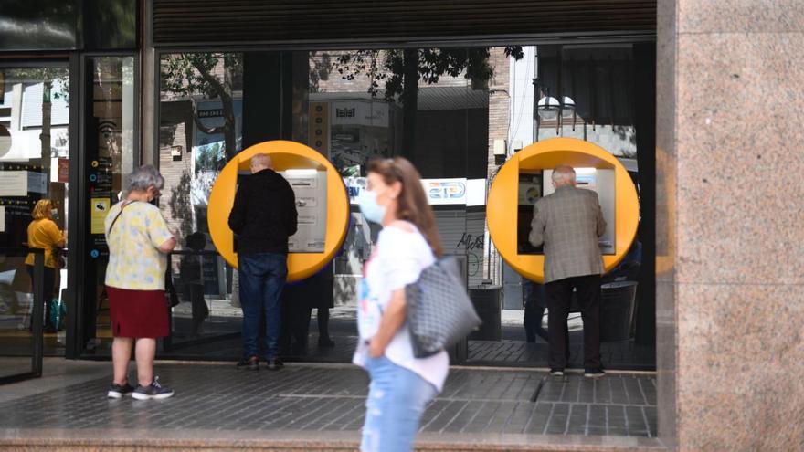 Oficina de una entidad bancaria en tiempos de pandemia, con usuarios en los cajeros. | // JORDI COTRINA