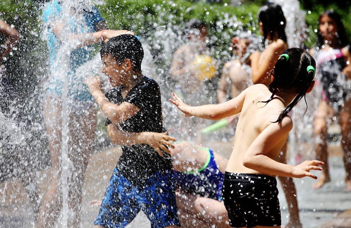 Niños que participan en las colonias de un casal del barrio barcelonés de Horta, se refrescan en una fuente.