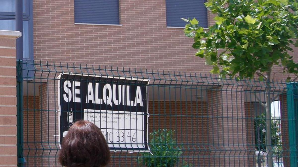 Una mujer mira un cartel de una vivienda en alquiler.
