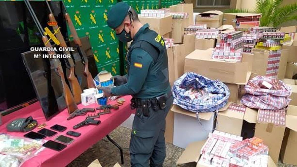 Un agente de la Guardia Civil junto a las armas y tabaco intervenidos en la operación.