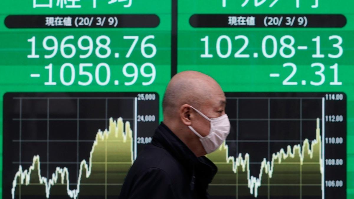 El temor al avance del coronavirus causa un lunes negro en las bolsas asiáticas. En la foto, un ciudadano con mascarilla pasa frente a un cartel con información del índice Nikkei, en Tokio.