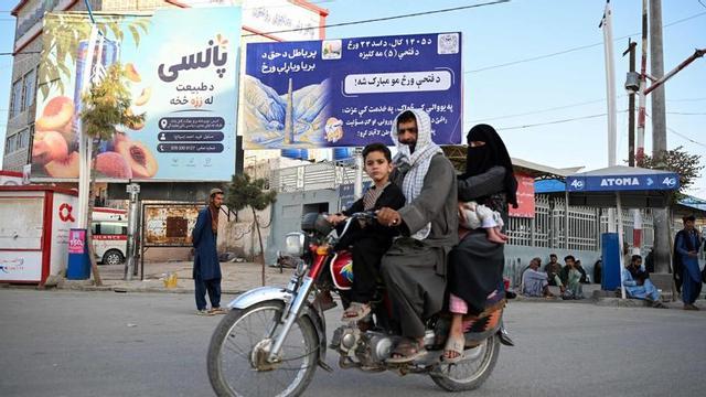 Una família afganesa passa amb moto davant un cartell amb missatges del Govern talibà a Kandahar, ahir.  | SANAULLAH SEIAM / AFP