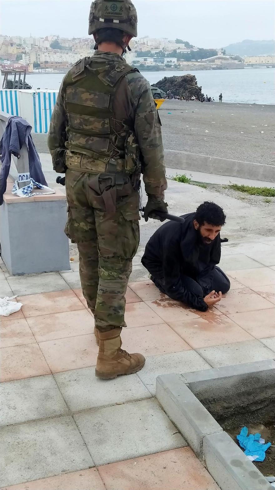 Un miembro del Ejército de Tierra observa a un inmigrante marroquí que ha cruzado la frontera a nado por los espigones fronterizos de Ceuta este martes.