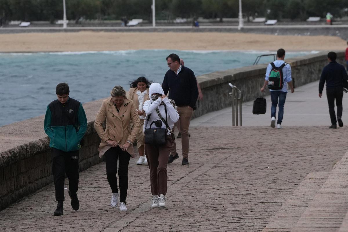 Varias personas caminan bajo la lluvia en la playa de Ondarreta, en San Sebastián.
