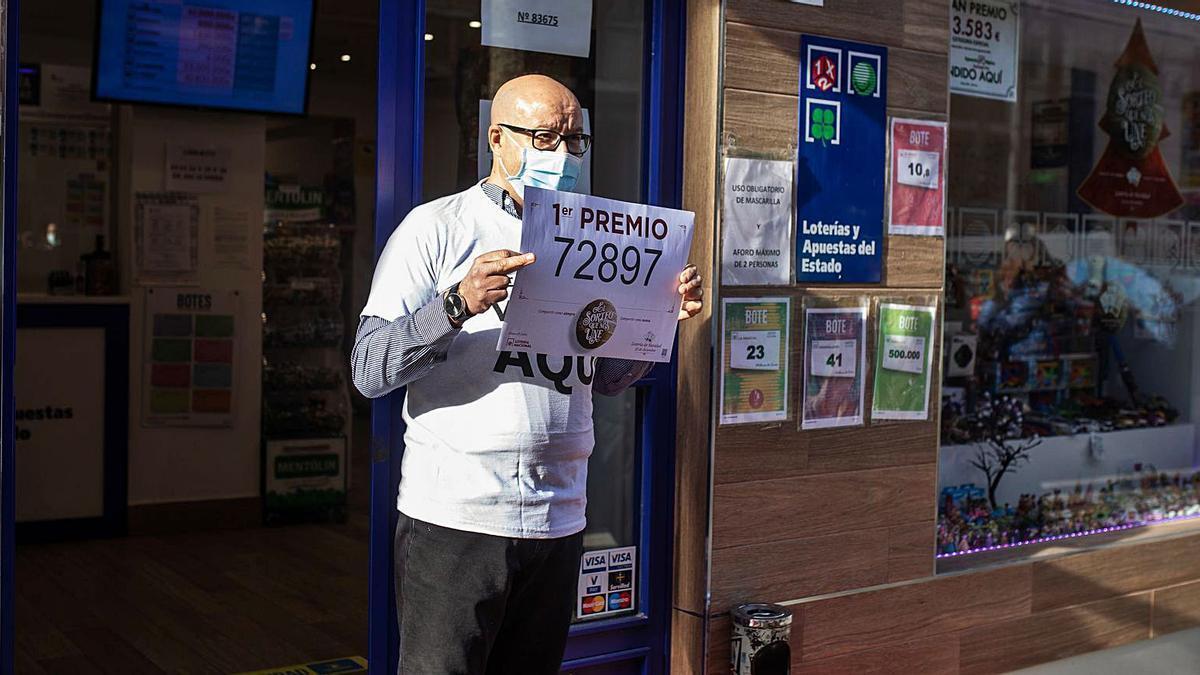 Martín González sujeta el cartel que acredita la venta de parte del primer premio de la Lotería de Navidad en su establecimiento.