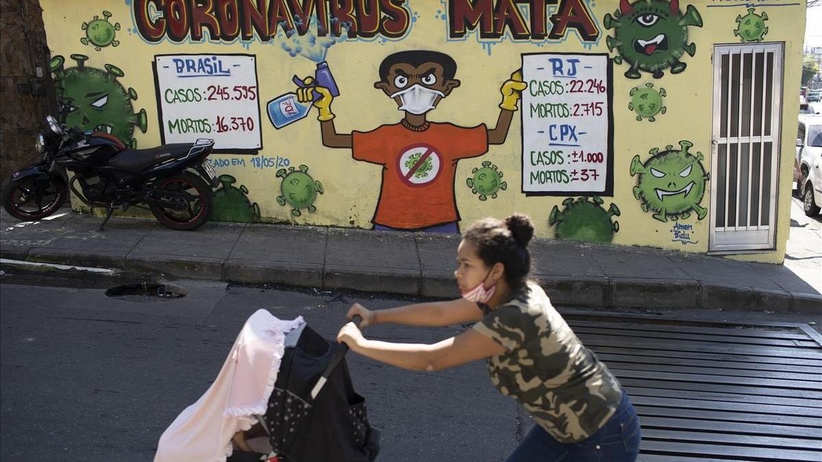 Una mujer empuja un carro de bebé ante un cartel que pide precaución frente al coronavirus en el Complexo do Alemão, una barriada de favelas en Rio de Janeiro.