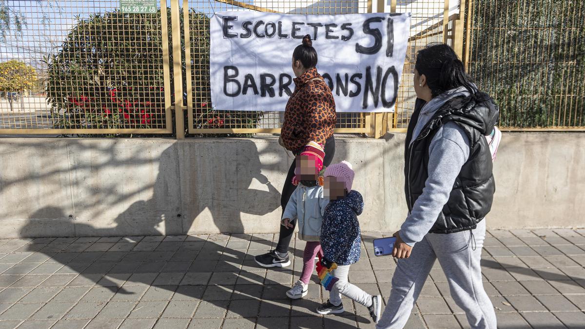 Madres pasan por delante de una pancarta colocada en Els Xiquets, donde se prevén instalar los barracones