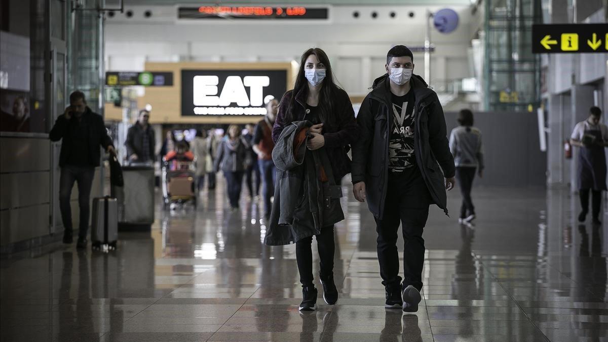 Pasajeros con mascarillas procedentes de Milán tras acceder al área de llegadas del aeropuerto de El Prat. 