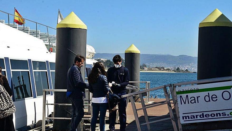 Persona y usuarios con masrcarillas en el pantalán de Cangas.