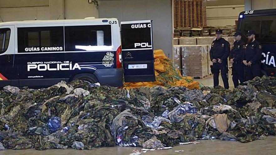 Agentes de la Policía Nacional custodian la montaña de ropa de camuflaje dentro del depósito aduanero del Puerto de Valencia.