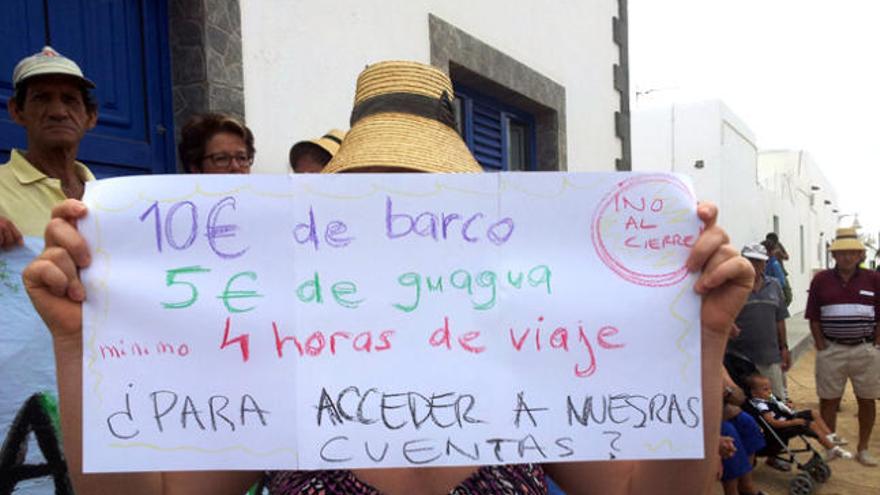 Una vecina con el cartel que relata lo que costará ir al banco en La Graciosa. | lp / dlp