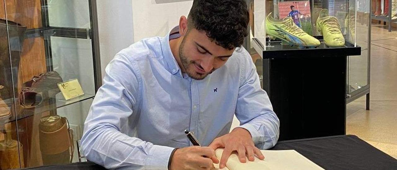 Sergio Ortuño firmando en el libro del Museo del Calzado con sus botas en la vitrina del fondo.