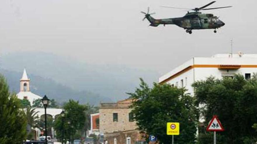 Una densa humareda cubre Sant Joan mientras un helicóptero militar vuela cerca de la iglesia.