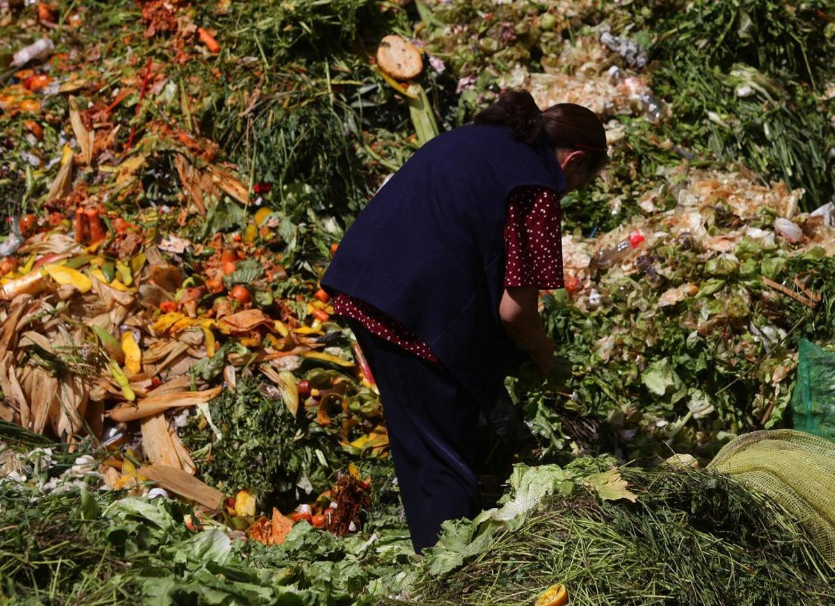 Una mujer busca alimentos entre la basura de un mercado de abastos.