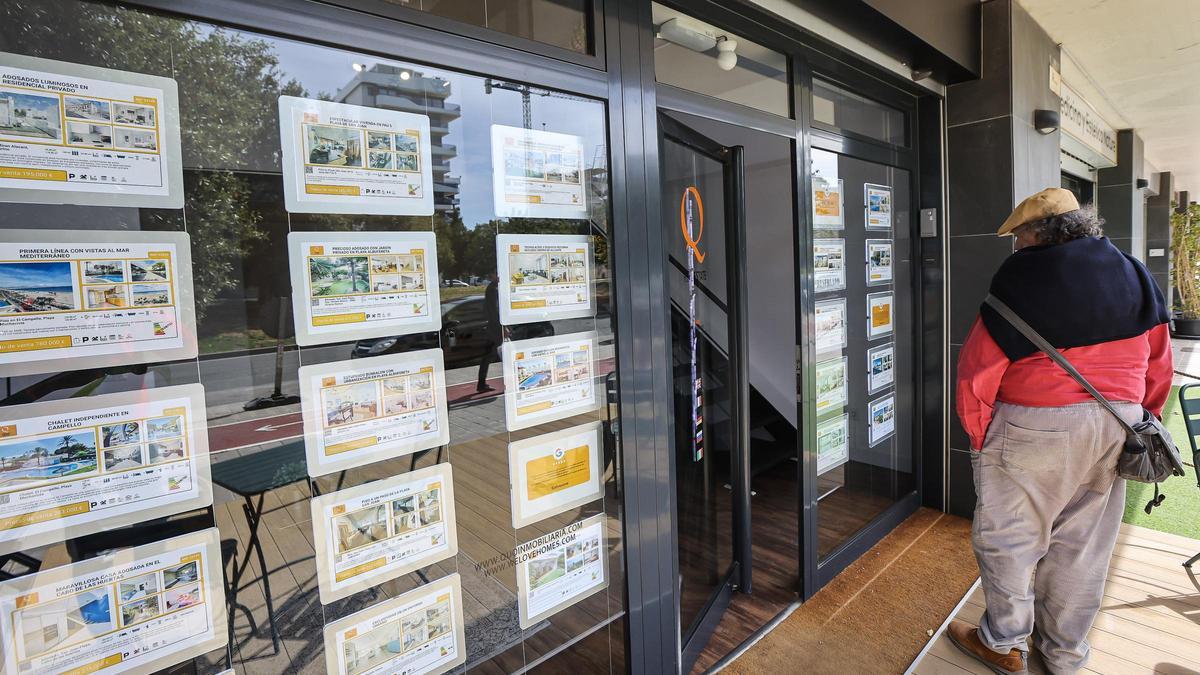 Un interesado mira las viviendas que se ofrecen en una inmobiliaria alicantina.