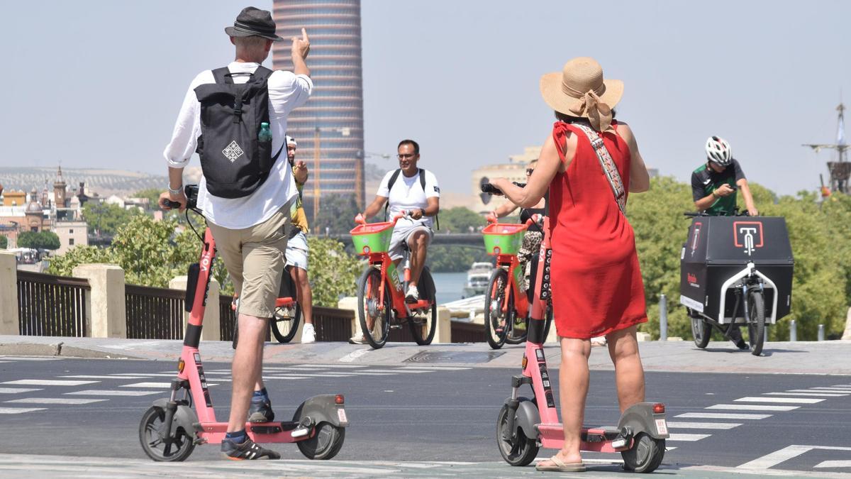 Turistas haciendo uso de patinetes eléctricos por Sevilla. El Ayuntamiento no descarta eliminarlos